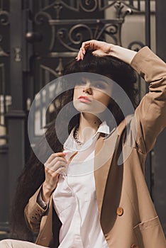 Close up portrait of young beautiful woman with long brunette curly hair posing against building background. sitting on