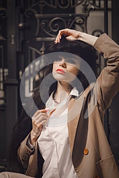 Close up portrait of young beautiful woman with long brunette curly hair posing against building background. sitting on