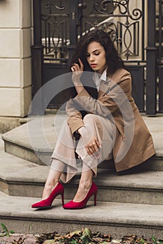 Close up portrait of young beautiful woman with long brunette curly hair posing against building background. sitting on