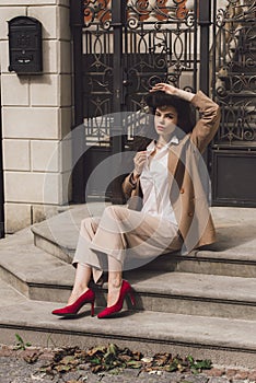 Close up portrait of young beautiful woman with long brunette curly hair posing against building background. sitting on