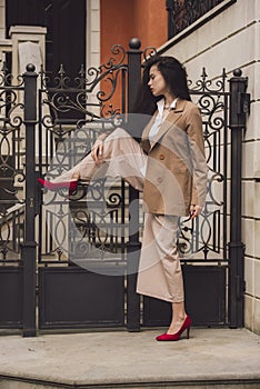 Close up portrait of young beautiful woman with long brunette curly hair posing against the metal fence of the cottage