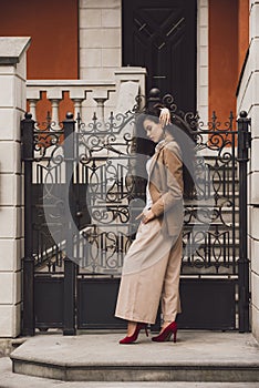 Close up portrait of young beautiful woman with long brunette curly hair posing against the metal fence of the cottage