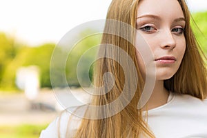 Close-up portrait of a young blonde girl in casual clothes in a green park. Lifestyle concept