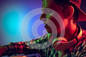 Close-up portrait of young boy with headphones making sounds with professional dj mixer isolated over blue background in