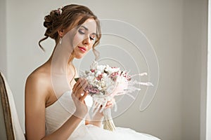 Close up portrait of young bride in a beautiful dress holding a bouquet of flowers in bright white studio. Wedding