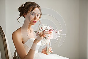 Close up portrait of young bride in a beautiful dress holding a bouquet of flowers in bright white studio. Wedding