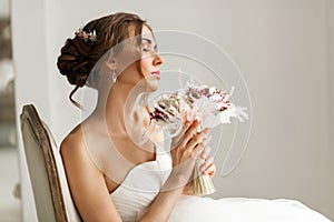 Close up portrait of young bride in a beautiful dress holding a bouquet of flowers in bright white studio. Wedding