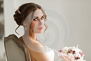 Close up portrait of young bride in a beautiful dress holding a bouquet of flowers in bright white studio. Wedding