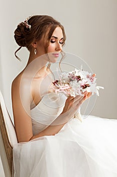 Close up portrait of young bride in a beautiful dress holding a bouquet of flowers in bright white studio. Wedding