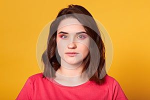 Close up portrait of young brunette girl with bright make up looking directly at camera. Eyelids colored in pink and orange, model