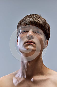 Close up portrait of young, calm brunette man with bare shoulders looking away isolated over grey studio background.