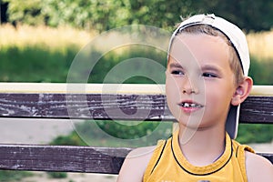 Close up portrait of young caucasian boy sitting on bench at the park.