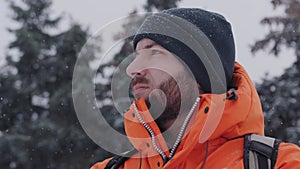 Close up or a portrait of a young caucasian man looking in distance and warming his hands up on a snowy winter day