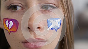 Close-up portrait of young caucasian woman with painted social media icons on her face looking at camera. Addiction to
