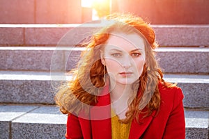 Close-up portrait young caucasian woman with red curly hair in red coat in wind