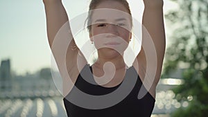 Close-up portrait of young charming Caucasian woman raising hands and smiling at camera in sunlight. Beautiful brunette