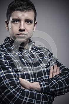 Close up portrait of young composed man wearing checked shirt with arms crossed