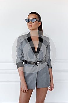 Close up portrait of a young confident girl in grey jacket with sunglasses, looking at the side, over white background