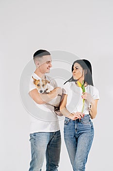 Close up portrait young couple hugging, holding yellow flowers and dog in studio on white background. couple embracing