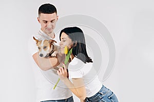 Close up portrait young couple hugging, holding yellow flowers and dog in studio on white background. couple embracing