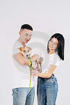 Close up portrait young couple hugging, holding yellow flowers and dog in studio on white background. couple embracing