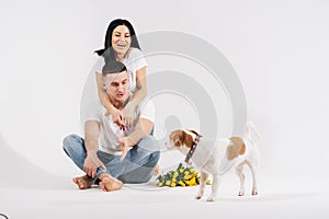 Close up portrait young couple sit and hugging, holding yellow flowers and dog in studio on white background. couple