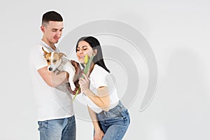 Close up portrait young couple with yellow flowers and dog isolated on white background. lovely couple embracing with