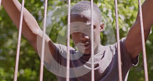 Close up portrait of young desperate african american guy standing behind metal bars outdoors