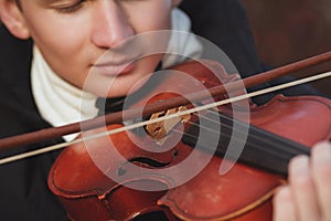 Close-up portrait of a young elegant man playing the violin on autumn nature backgroung, boy`s face with musical instrument under