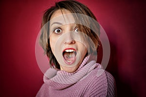 Close-up portrait of young emotional woman with short hair dressed in pink sweater is posing in the studio on bright