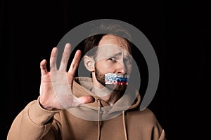 Close-up portrait of young emotive man with three colors duct tape over his mouth isolated on dark background