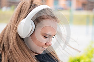 Close-up portrait of a young fat woman with headphones. Beautiful chubby girl listening to music outdoors