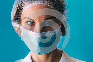 Close-up portrait of young female doctor in medical cap and white gown on blue background with space for text.