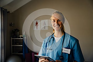 Close up portrait of young female doctor with scrubs with tablet, smiling and happy