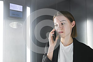Close-up portrait of a young female office worker talking on her phone in the elevator. Attractive businesswoman is using her