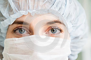 Close-up portrait of young female surgeon doctor or intern wearing protective mask and hat