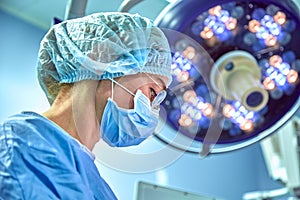 Close up portrait of young female surgeon doctor wearing protective mask and hat during the operation. Healthcare