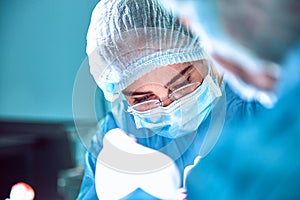 Close up portrait of young female surgeon doctor wearing protective mask and hat during the operation. Healthcare