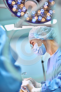 Close up portrait of young female surgeon doctor wearing protective mask and hat during the operation. Healthcare