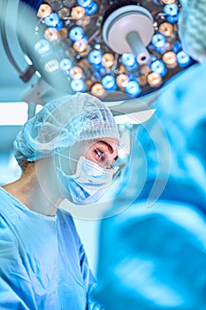 Close up portrait of young female surgeon doctor wearing protective mask and hat during the operation. Healthcare