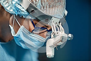 Close up portrait of young female surgeon doctor wearing protective mask and hat during the operation. Healthcare