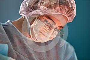 Close up portrait of young female surgeon doctor wearing protective mask and hat during the operation. Healthcare