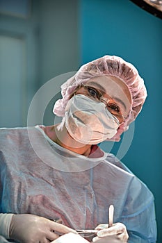 Close up portrait of young female surgeon doctor wearing protective mask and hat during the operation. Healthcare