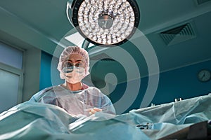 Close up portrait of young female surgeon doctor wearing protective mask and hat during the operation. Healthcare