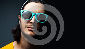 Close-up portrait of young guy wearing cyan sunglasses on black background with copy space.