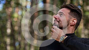 Close-up portrait of young handsome Caucasian man yawning looking around standing in sunny forest in the morning. Happy