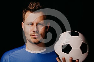 Close-up portrait of young handsome football player soccer posing on dark background.