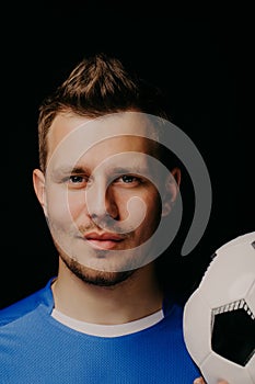 Close-up portrait of young handsome football player soccer posing on dark background.