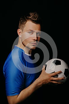 Close-up portrait of young handsome football player soccer posing on dark background.