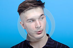 Close up portrait of young handsome man with astonished grimace on blue background.  Fashion hairstyle, strong emotions, expressiv
